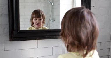 Uzun saçlı komik anaokulu çocuğu, yüzünü aynaya çekiyor.