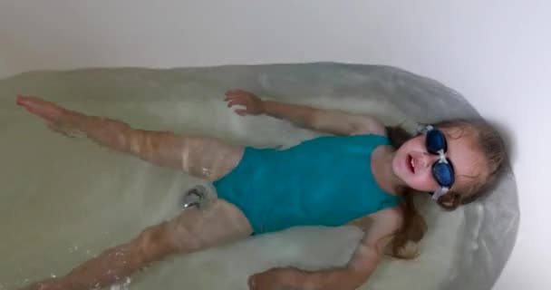 Funny girl in blue diving glasses and swimsuit swims in bath — Stock Video