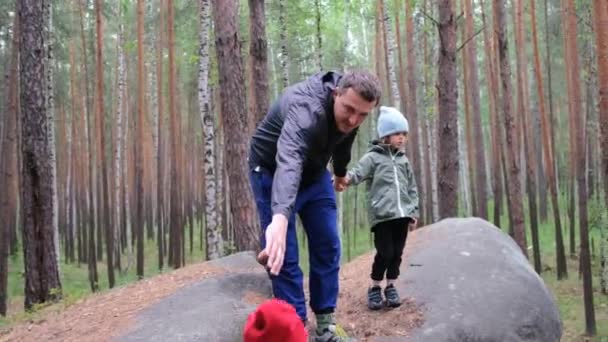 El padre ayuda a los niños con chaquetas de colores a trepar por grandes rocas — Vídeo de stock