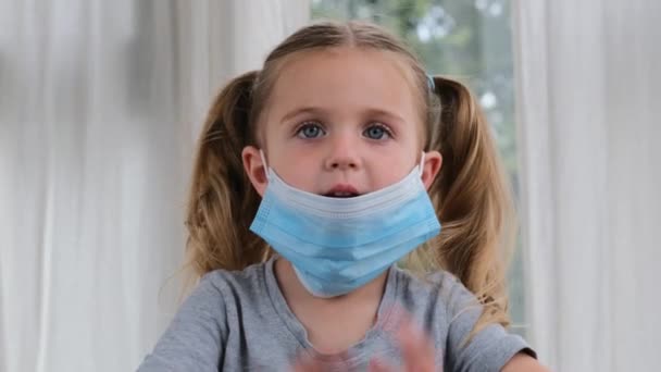 Syg lille pige iført en medicinsk maske mod virus closeup lokking på kamera – Stock-video