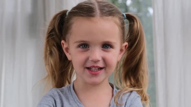 Смешная маленькая девочка улыбается, глядя в камеру дома — стоковое видео