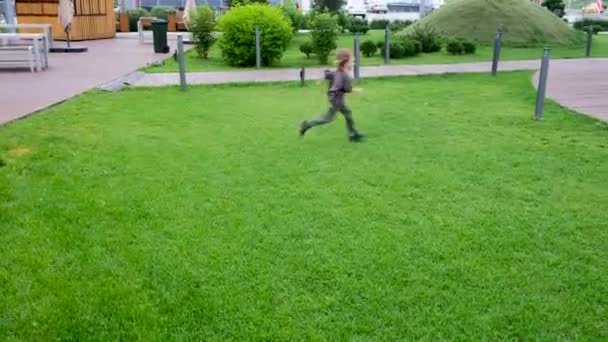 लांब केस असलेला मोठा मुलगा आणि तरुण मुलगी हिरव्या गवत बाजूने धावा — स्टॉक व्हिडिओ