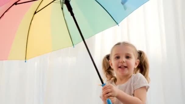 Игривая маленькая девочка в серой футболке позирует с открытым зонтиком — стоковое видео
