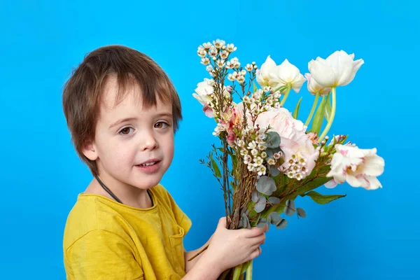 Charmig pojke med ljusa blommande blommor på blå bakgrund — Stockfoto
