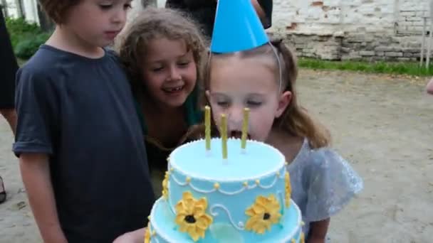 Funny little girl bites birthday cake with candles at party — Stock Video