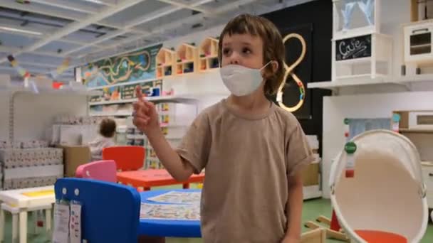 Mały chłopiec w masce ochronnej gesty zabawy w sklepie z zabawkami — Wideo stockowe