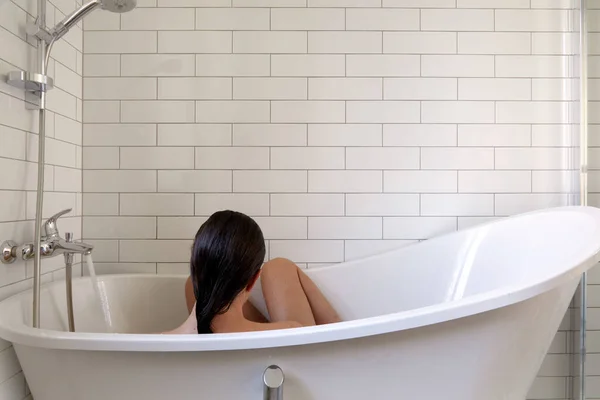 Mulher tomando banho na banheira no banheiro branco — Fotografia de Stock