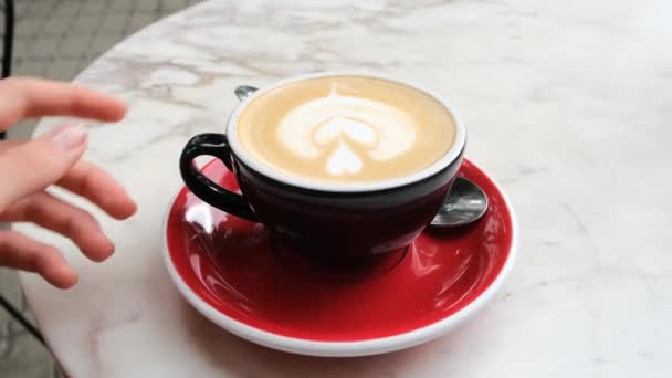 Kobieta bierze filiżankę kawy z rysunkiem mleka z czerwonego spodka — Wideo stockowe
