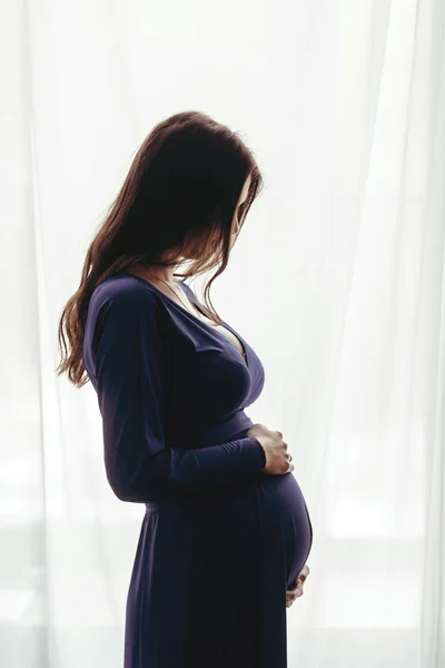 Wanita hamil berdiri melawan jendela — Stok Foto
