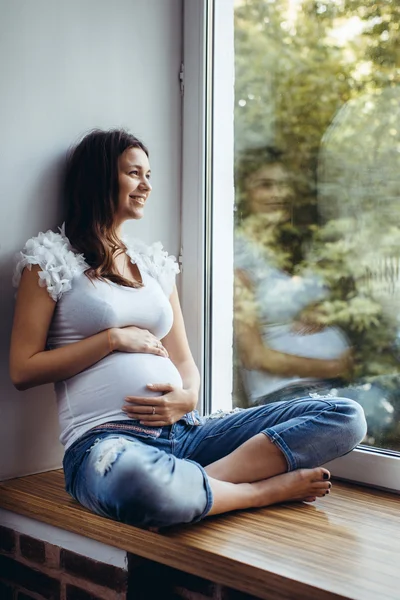 Menina morena grávida sentada no peitoril da janela — Fotografia de Stock