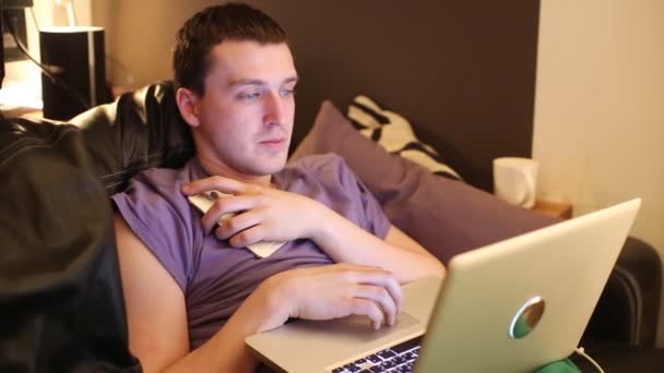 Чоловік зі смартфоном і ноутбуком на дивані — стокове відео