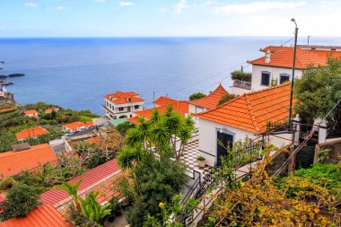 Portekiz, Madeira 'da kırmızı çatıları ve okyanusu olan Camara de Lobos köyünün panoraması