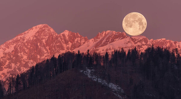 Full moon setting behind the mountains at sunrise. and presenting an beautiful scene
