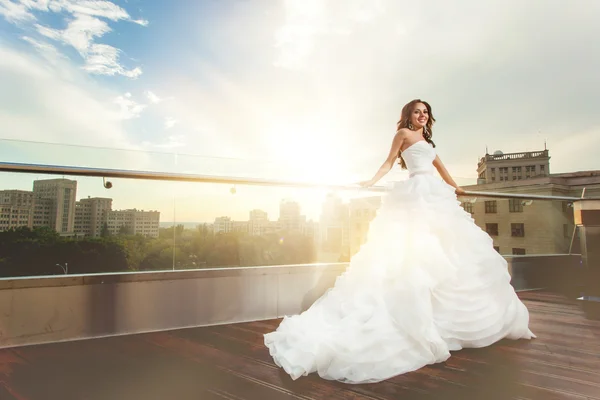 Mujer novia en vestido de novia y puesta de sol sobre la ciudad moderna detrás —  Fotos de Stock