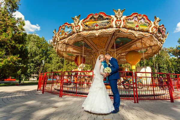 Nevěsta a ženich v parku poblíž kolotoč — Stock fotografie