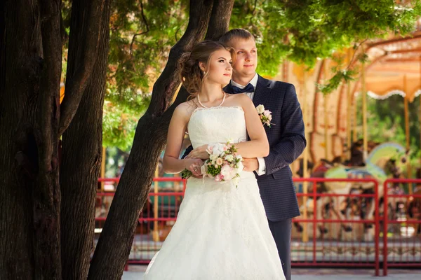 Wedding couple near carousel and tree — Stock Photo, Image