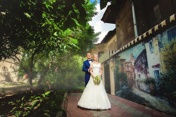 Brudgummen bakom bruden i park nära vackra byggnad — Stockfoto