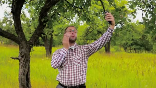 Hombre en gafas que se quedan en el prado y haciendo selfie divertido — Vídeos de Stock