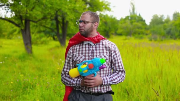 Hombre en manto rojo apuntando y disparando con pistola de juguete en el campo — Vídeo de stock