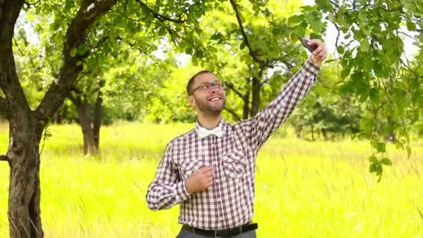 Młody człowiek w okularach co selfie na łące i śmiejąc się — Wideo stockowe