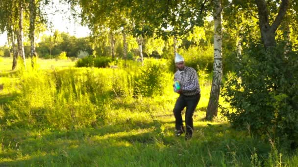 Junger Mann mit Kapuze schleicht langsam mit Spielzeugpistole durch den Wald — Stockvideo