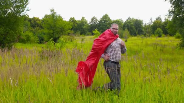 Νεαρός άνδρας με κόκκινο μανδύα, τρέχει μέσα από το πεδίο και να επιστρέφουν αργά — Αρχείο Βίντεο