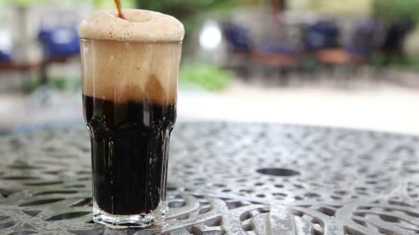 Ein volles Glas schaumiges dunkles Bier, das auf einem Tisch steht und durch die Decke fließt — Stockvideo