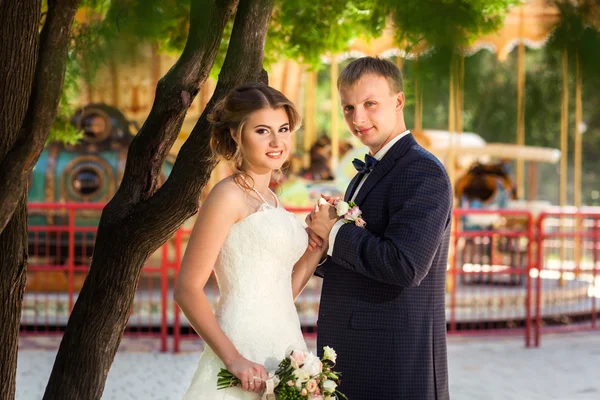 Bruid en bruidegom in de buurt van boom en carrousel — Stockfoto