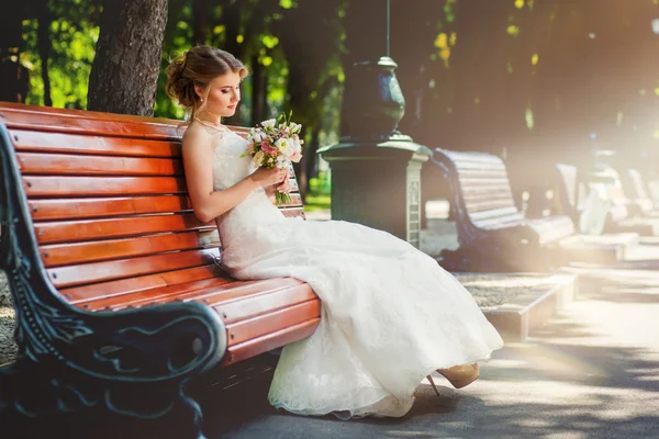 Mariée avec bouquet sur banc à l'ancienne dans le parc — Photo