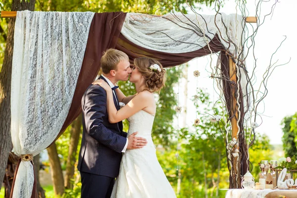 Paar küsst sich unter dekorativem Hochzeitsbogen — Stockfoto