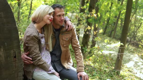 Пара сидящих возле большого бревна и целующихся — стоковое видео