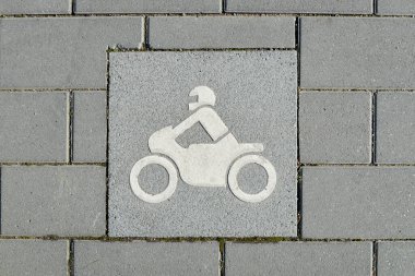 Otoparkın logosu bir motosiklet için ayrılmış, stilize edilmiş bir motosiklet üzerindeki silüet ile resmedilmiş, çimento kiremit üzerine kazınmış bir adam.