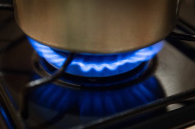 Ocağın üstünde paslanmaz çelik bir tavanın altında mavi alevlerin yakın çekimi.