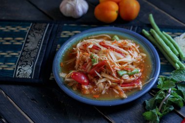 Baharatlı papaya salatası mavi bir tabakta, kovada pilav ve uzun fasulye, kurutulmuş kırmızı biber ve sebze ile servis edilir..