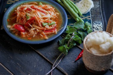 Baharatlı papaya salatası mavi bir tabakta, kovada pilav ve uzun fasulye, kurutulmuş kırmızı biber ve sebze ile servis edilir..