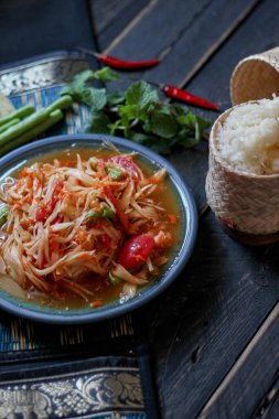 Baharatlı papaya salatası mavi bir tabakta, kovada pilav ve uzun fasulye, kurutulmuş kırmızı biber ve sebze ile servis edilir..