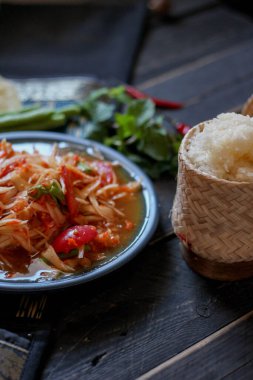 Baharatlı papaya salatası mavi bir tabakta, kovada pilav ve uzun fasulye, kurutulmuş kırmızı biber ve sebze ile servis edilir..