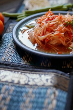 Baharatlı papaya salatası mavi bir tabakta, kovada pilav ve uzun fasulye, kurutulmuş kırmızı biber ve sebze ile servis edilir..