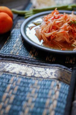 Baharatlı papaya salatası mavi bir tabakta, kovada pilav ve uzun fasulye, kurutulmuş kırmızı biber ve sebze ile servis edilir..