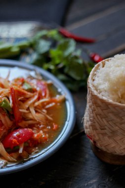 Baharatlı papaya salatası mavi bir tabakta, kovada pilav ve uzun fasulye, kurutulmuş kırmızı biber ve sebze ile servis edilir..