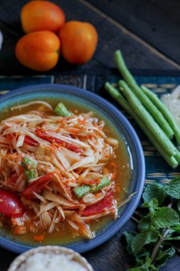 Baharatlı papaya salatası mavi bir tabakta, kovada pilav ve uzun fasulye, kurutulmuş kırmızı biber ve sebze ile servis edilir..