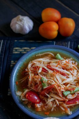 Baharatlı papaya salatası mavi bir tabakta, kovada pilav ve uzun fasulye, kurutulmuş kırmızı biber ve sebze ile servis edilir..
