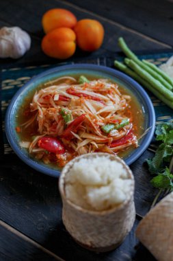 Baharatlı papaya salatası mavi bir tabakta, kovada pilav ve uzun fasulye, kurutulmuş kırmızı biber ve sebze ile servis edilir..