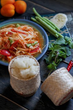 Baharatlı papaya salatası mavi bir tabakta, kovada pilav ve uzun fasulye, kurutulmuş kırmızı biber ve sebze ile servis edilir..