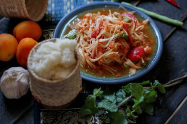 Baharatlı papaya salatası mavi bir tabakta, kovada pilav ve uzun fasulye, kurutulmuş kırmızı biber ve sebze ile servis edilir..