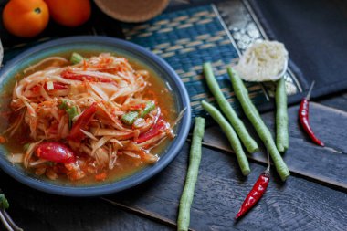 Baharatlı papaya salatası mavi bir tabakta, kovada pilav ve uzun fasulye, kurutulmuş kırmızı biber ve sebze ile servis edilir..