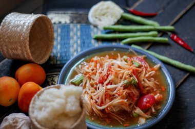 Baharatlı papaya salatası mavi bir tabakta, kovada pilav ve uzun fasulye, kurutulmuş kırmızı biber ve sebze ile servis edilir..