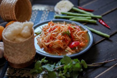 Baharatlı papaya salatası mavi bir tabakta, kovada pilav ve uzun fasulye, kurutulmuş kırmızı biber ve sebze ile servis edilir..