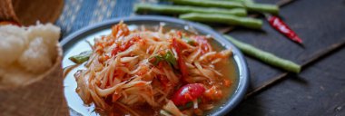 Baharatlı papaya salatası mavi bir tabakta, kovada pilav ve uzun fasulye, kurutulmuş kırmızı biber ve sebze ile servis edilir..