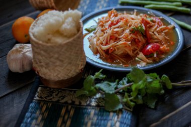 Baharatlı papaya salatası mavi bir tabakta, kovada pilav ve uzun fasulye, kurutulmuş kırmızı biber ve sebze ile servis edilir..